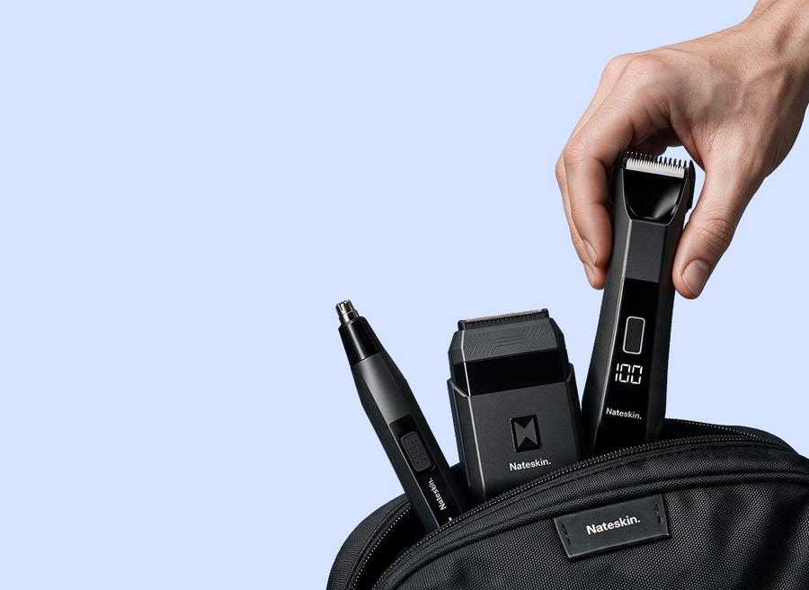 A hand inserts a black Nateskin hair clipper into a black zippered bag, alongside a matching trimmer and a black hair removal head, on a light blue background.